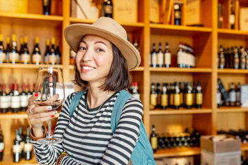 Happy asian Woman sniffing and tasting red wine in a glass in winery shop