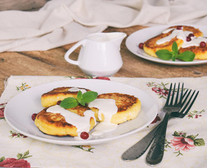 Frying cottage cheese pancakes with oat-flakes. Ukrainian or russian syrniki with jam and sour cream on wooden background. Traditional breakfast. Gluten free.