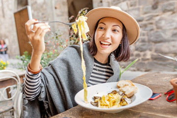 Happy asian woman eating pasta with truffle in outdoor italian restaurant