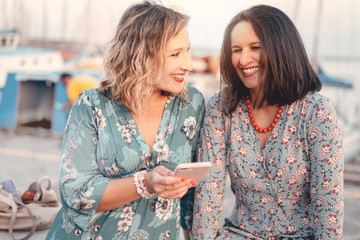 Two women friends laughing while watching the smartphone screen