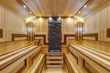 Inside in big Russian bath. Interior of wooden sauna in light and dark colors with bench, many little lamp on ceiling. Hot stones and bucket of water. Health care.