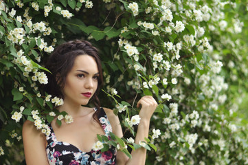 Young beautiful dark-haired woman in color dress with open shoulders in bright green blooming...
