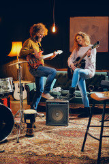 Caucasian woman playing acoustic guitar while man playing bass. Home studio interior.
