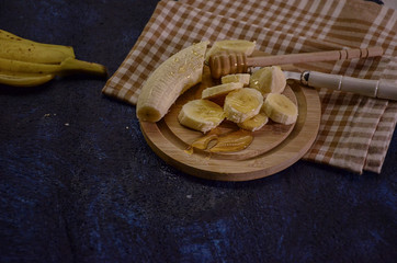 Banana slices on a plate with honey being poured onto banana. Healthy snack concept on blue background