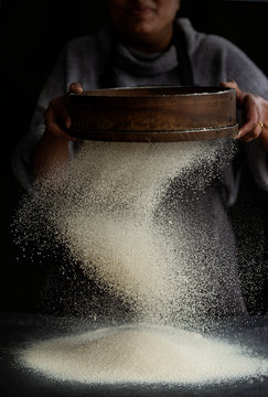 Midsection of baker sieving flour on kitchen countertop