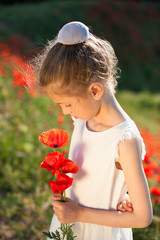 pensive little pretty girl in white summer dress with bouquet of poppy flowers