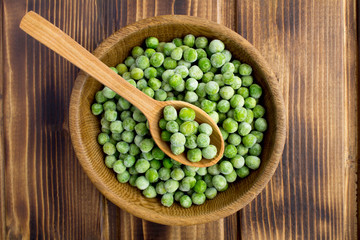 Frozen peas  in the brown bowl  on the wooden background.Top view.Healthy food ingredient.