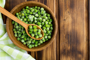 Frozen peas  in the brown bowl  on the wooden background.Top view.Healthy food ingredient.