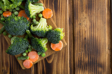 Frozen vegetables in the cutting board on the brown  wooden background.Top view.Copy space.Healthy food ingredients.