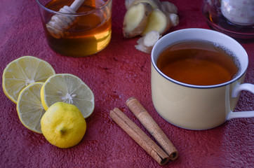  Healthy winter drink concept. Antiviral useful drink ginger tea with lemon, honey and slices of ginger on wooden red and orange background.