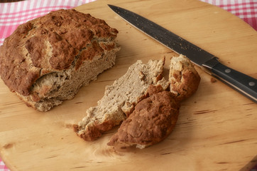 Healthy eating concept. Homemade bread put on kitchen wood plate with a chef holding knife for cut. Fresh bread on table close-up. Fresh bread on the kitchen table with pink cloth