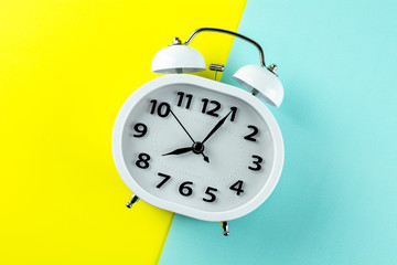 white vintage alarm clock on yellow and blue background. - top view.