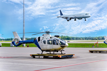 Fototapeta na wymiar Helicopter chopper at airport with a jet taking off on background of blue sky.