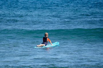 little boy lies on a surfboard in the blue sea. view from the shore.