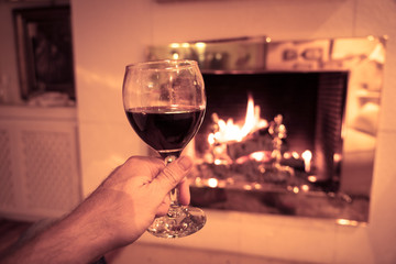 Close up of happy man drinking wine relaxing by fire place at home in winter holidays vacation
