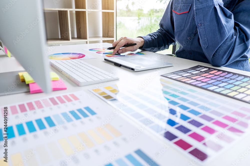 Poster Image of male creative graphic designer working on color selection and drawing on graphics tablet at workplace with work tools and accessories