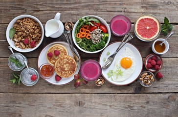 Brunch or breakfast table. Festive brunch set, meal variety with quinoa salad bowl, fried egg, granola, pankes, chia seeds pudding and smoothy  . Overhead view