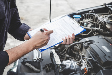 Fototapeta na wymiar Services car engine machine concept, Automobile mechanic repairman checking a car engine with inspecting writing to the clipboard the checklist for repair machine, car service and maintenance