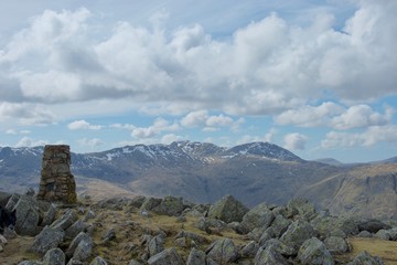 Cairn and rocks at summit of Lake District mountain; snow covered crags in distance