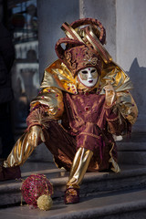 Fototapeta premium Person in carnival costume of Harlequin sits on the steps in the street in Venice, Italy