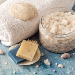 Large crystals of sea salt in a round transparent jar, next to a towel and seashells.