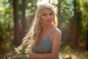 Young beautiful blonde woman in blue sexy dress - neglegee pegnoir underwear posing in forest in summer