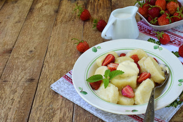 Sweet lazy pierogi. Ukrainian dumplings with sour cream, butter and strawberry on wooden background. Summer berry breakfast. Italian gnocchi. Copy space