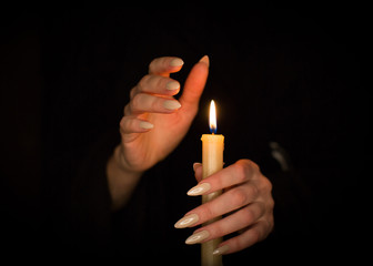 Candle and female witch hands with sharp pearl nails. Divination and witchcraft, low key.