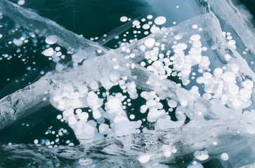 Beautiful unusual winter natural background with white bubbles of bottom gases in the clear ice of frozen Baikal lake