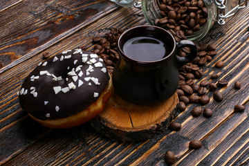 Donut with black icing and chocolate powder and an authentic cup of strong coffee. A can of coffee beans and poured grains.