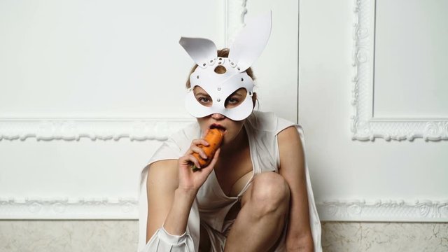 Beautiful Sexy Bunny Girl. Young woman in bunny leather mask eat carrot on white vintage background. Sexy easter bunny girl.