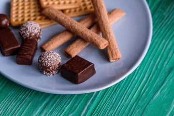 Shortbread cookies and chocolates on a btruzy plate, standing on a green wooden background.