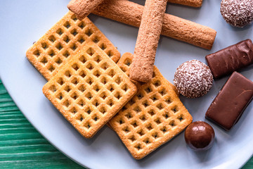 Shortbread cookies and chocolates on a btruzy plate, standing on a green wooden background.