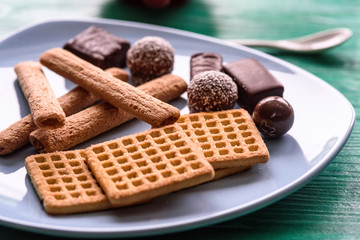 Shortbread cookies and chocolates on a btruzy plate, standing on a green wooden background.