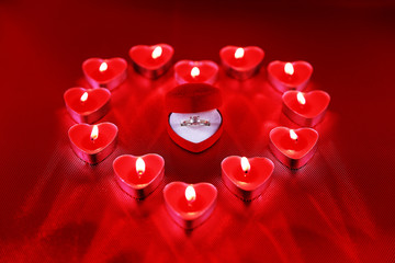 Wedding solitaire ring in heart shaped red box with heart shaped candle on red background. Valentine's day concept.