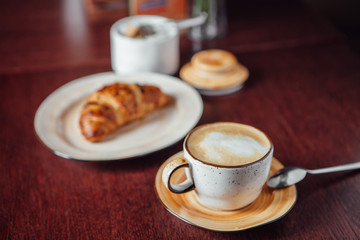 Croissant dusted with chocolate chips and a cup of coffee on a table of dark wood in the bar