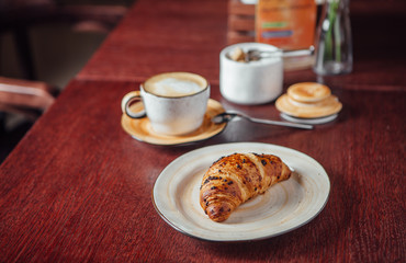 Croissant dusted with chocolate chips and a cup of coffee on a table of dark wood in the bar