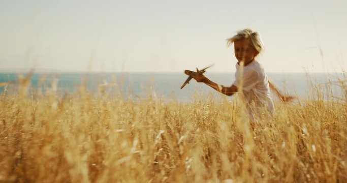 Adorable young boy running through golden field holding wooden airplane