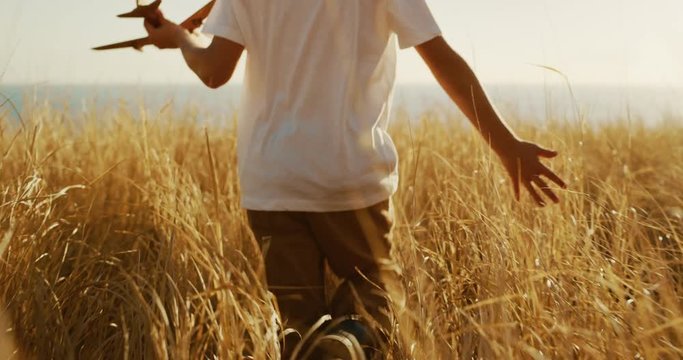 Young boy walking and running his hand through golden grass at sunset