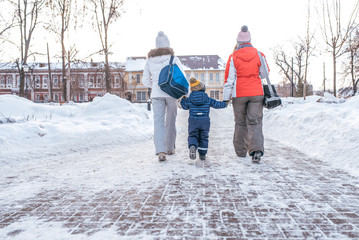 Fototapeta na wymiar Two girlfriends mom escort small child boy 2-4 years. Women parents Hold hands, go in the winter in the city along the snow-covered pavement, escorted to house, view from the rear.