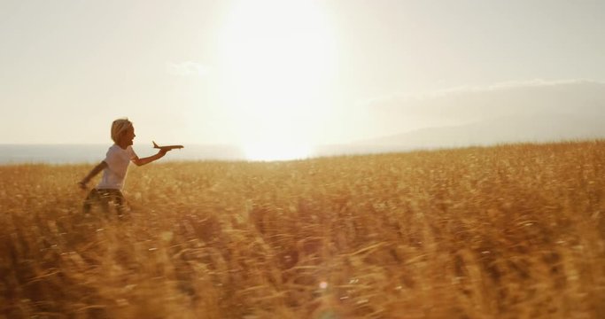 Adorable young boy running through golden field holding wooden airplane - Powered by Adobe