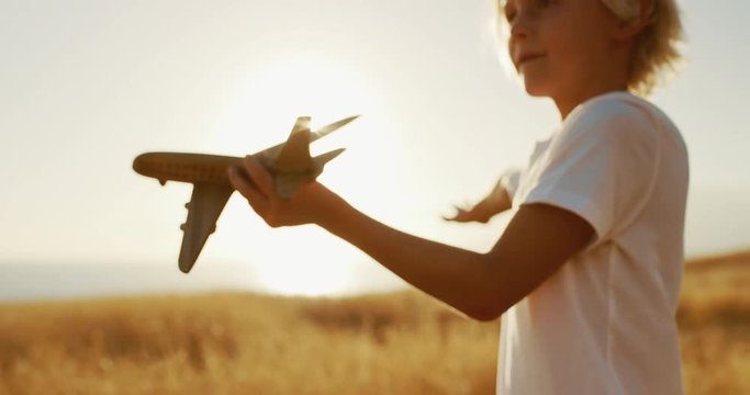 Happy young boy flying his wooden toy airplane in golden field at sunset