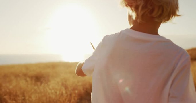 Happy young boy flying his wooden toy airplane in golden field at sunset