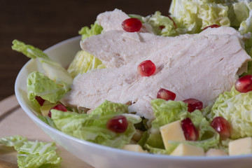 Food photography concept - close up of plate of salad with boiled chicken meat, cheese, green salad leaves on wooden background
