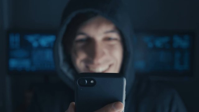 Happy Hacker in the hood uses a smartphone in a secret data center filled with screens