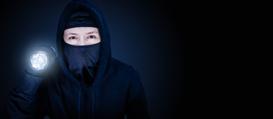 Panorama Einbrecher mit Sturmmaske und Taschenlampe auf blau schwarzen Hintergrund