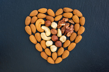 Assorted nuts heart shaped on dark background.