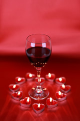 Valentine's day, glass of wine with heart shaped candles on red background.