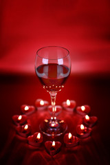 Naklejka na ściany i meble Valentine's day, glass of wine with heart shaped candles on red background.