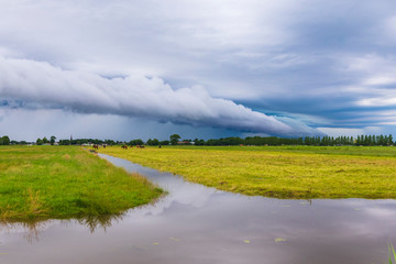 Shelf cloud and thunderstorm passing above green farmland and water